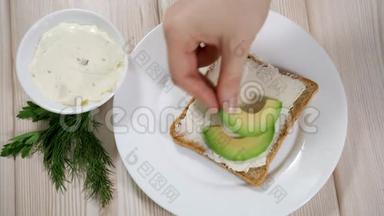 一位女士正在准备一份健康的早餐-烤面包，里面有大豆奶酪和鳄梨。 健康早餐概念，素食